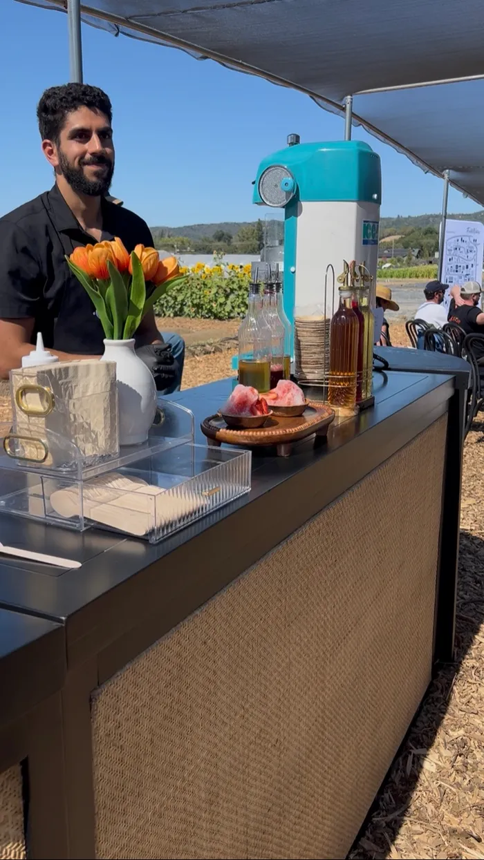 Tropics Shave Ice equipment, syrups, and tulips set up on a venue's black bar